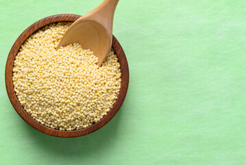 Yellow millet grain in wooden bowl with spoon on green background, Food ingredient, Top view