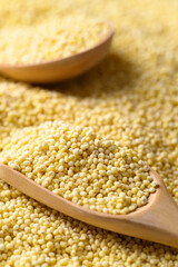 Yellow millet grain in wooden spoon, Food ingredient