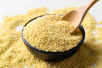 Yellow millet grain in black bowl with spoon, Food ingredient