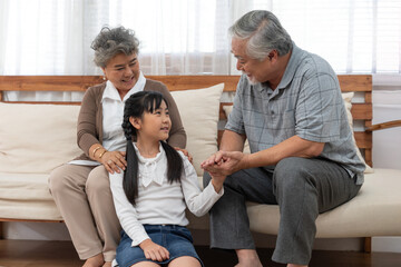 Happy Asian grandparents enjoying warm moment with their young granddaughter at home, sitting together and sharing smiles