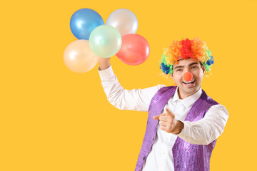 Happy young man in clown costume with balloons on yellow background