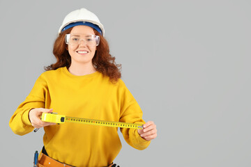 Female construction worker with measuring tape on grey background