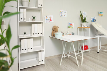 Interior of pediatrician's office with table, shelf unit and children's drawings