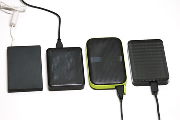 Four external hard drives with different designs and textures connected via USB cables on a white background. Portable storage devices for digital data, files, and backups.