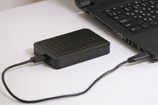 Close-up of an external hard drive connected to a laptop on a white table. Portable storage solution for digital files, data backup, and safe information transfer in modern technology.