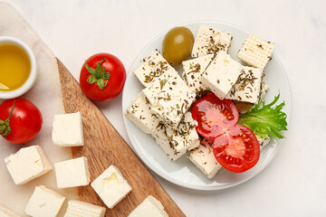 Plate with delicious cut feta cheese, olive and tomatoes on white grunge background