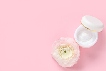 Jar of cream and ranunculus flower on pink background