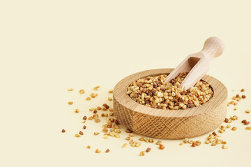 Wooden bowl and scoop with raw buckwheat grains on beige background