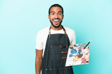 Young artist latin man holding a palette isolated on blue background with surprise facial expression