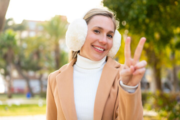 Young blonde woman wearing winter muffs at outdoors smiling and showing victory sign