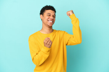 Young African American man isolated on blue background celebrating a victory