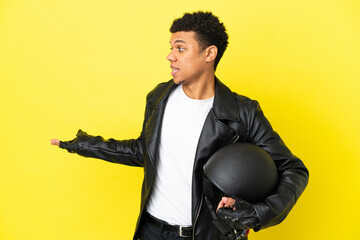 Young African American man with a motorcycle helmet isolated on yellow background with surprise...