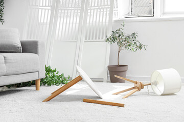 Broken table with overturned lamp on carpet in messy living room