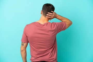 Young caucasian man isolated on blue background in back position and thinking