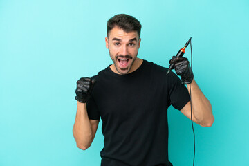Young tattoo artist man isolated on blue background celebrating a victory in winner position