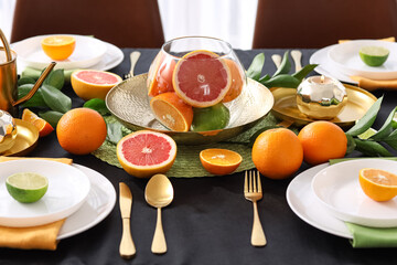 Beautiful table setting with citrus fruits, burning candle and black tablecloth in living room,...