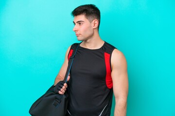 Young caucasian sport man with sport bag isolated on blue background looking to the side