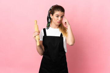 Young blonde woman holding a rolling pin isolated on pink background thinking an idea