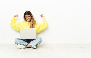 Young woman with a laptop sitting on the floor doing strong gesture
