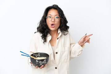 Young asian woman isolated on white background surprised and pointing side while holding a bowl of...