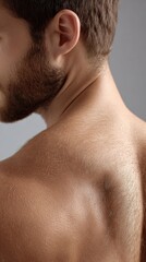 Naklejka premium Close-up of a man's shoulder and neck with short hair and beard against plain gray background, detailed skin texture and natural lighting