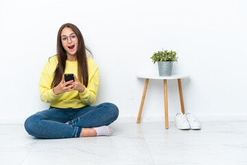 Young Ukrainian woman sitting on the floor of her house isolated on white wall surprised and...