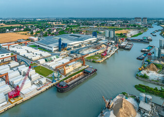 Aerial view of a precast concrete factory and industrial port with cranes loading barges on a river...