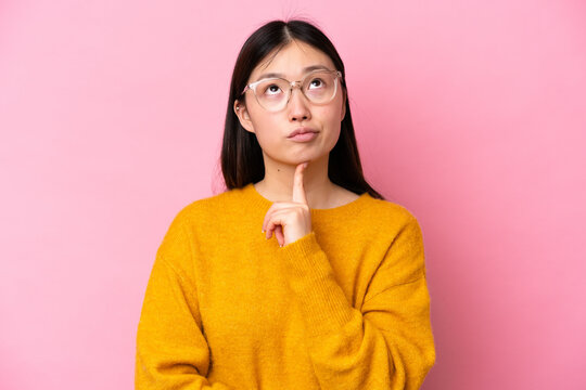 Young Chinese woman isolated on pink background With glasses and looking up