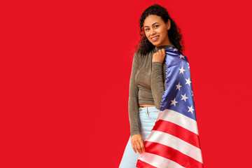 Beautiful young happy African-American woman with USA flag on red background