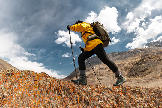 Girl trekker in hiking gear climbs a rock against the background of blue sky with clouds and rocky Altai mountains. Low angle bottom view. Adventure energy, endurance, solo hike