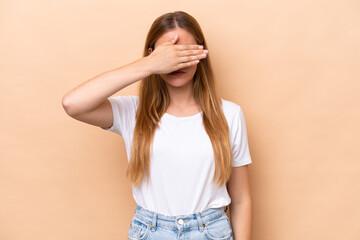 Young caucasian woman isolated on beige background covering eyes by hands. Do not want to see...