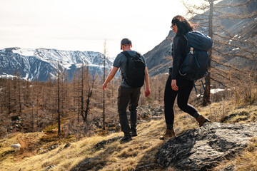 A couple of tourists with trekking backpacks descending a slope into a valley against the backdrop...