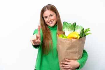 Young caucasian woman holding a grocery shopping bag isolated on white background showing and...