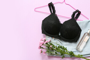 Composition with stylish female bra, jeans, bottle of perfume and flowers on lilac background