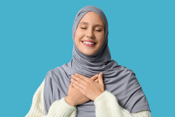 Thankful Muslim woman pressing hands to chest and smiling on blue background