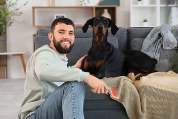 Young man with pet brush and Dobermann dog at home