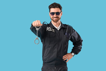 Happy male police officer with radio transmitter and handcuffs on blue background