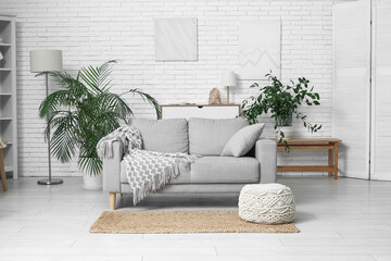 Interior of light living room with sofa and houseplants near white brick wall