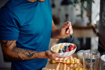 Close up of man eating oatmeal with fresh fruit in kitchen.