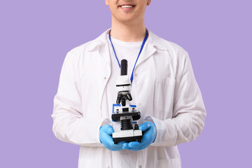 Young male scientist with microscope on lilac background, closeup