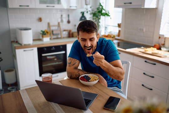 Happy man using laptop while having oatmeal for breakfast at dining table.