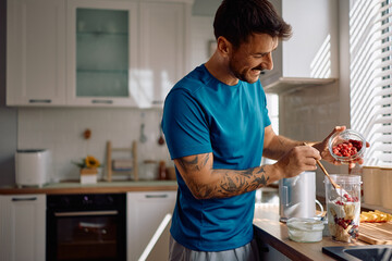 Happy man blending fresh fruit while making healthy breakfast in kitchen.