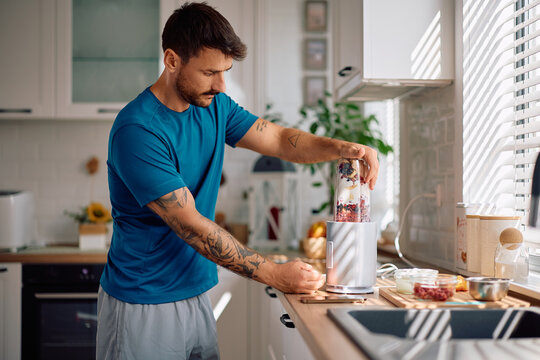 Mid adult man blending fresh fruit while preparing smoothie in morning. - Powered by Adobe