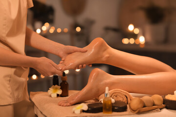 Female therapist massaging woman's foot in dark spa salon, closeup
