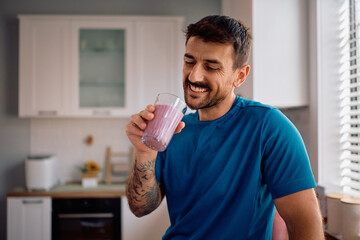 Happy man having glass of fresh fruit smoothie in morning.