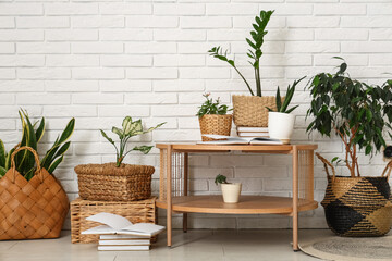 Table and wicker baskets with green plants near white brick wall in room