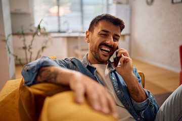 Happy man talking on mobile phone while relaxing in living room.