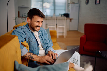 Happy man using laptop while relaxing on sofa.