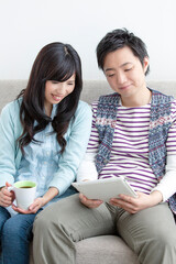 ソファでタブレットを見る夫婦