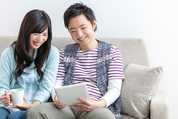 ソファでタブレットを見る夫婦